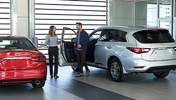 Man by silver INFINITI talking to woman at car dealership